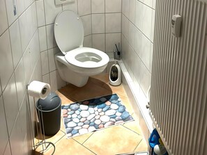 A small bathroom with a toilet, a bidet, a trash bin, and a toilet paper holder. - Cosy Apartment in Bad Harzburg With Garden (Bad Harzburg)