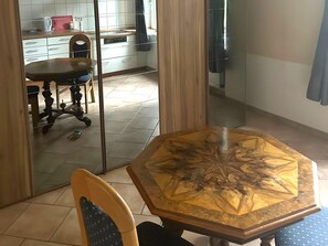 A dining area with a wooden table and chairs, a kitchen in the background, and a sliding glass door leading to another room. - Cosy Apartment in Bad Harzburg With Garden (Bad Harzburg)