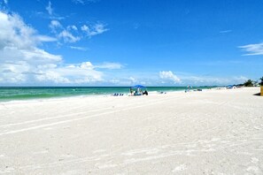 A wide sandy beach with a clear blue sky and calm sea.
