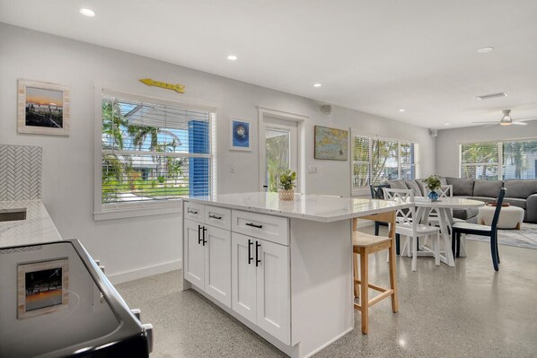 A modern kitchen with white cabinets, a central island, and a dining area with a white table and chairs.