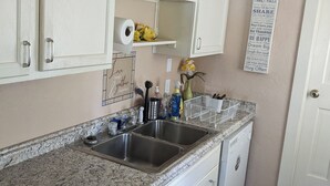 A kitchen with white cabinets, a granite countertop, a double sink, and a dish rack.