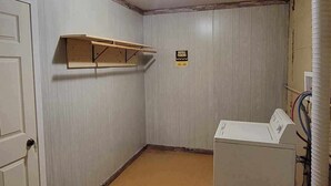 A laundry room with a washing machine, a bicycle parking sign, and a wooden shelf.