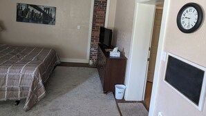 A bedroom with a bed, dresser, television, and a clock on the wall.