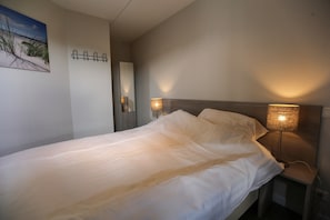 A neatly made bed with white linens, two bedside lamps, a wall-mounted mirror, and a framed picture of a beach scene. - Chalet in Gelderland With Hot Tub (Lathum)