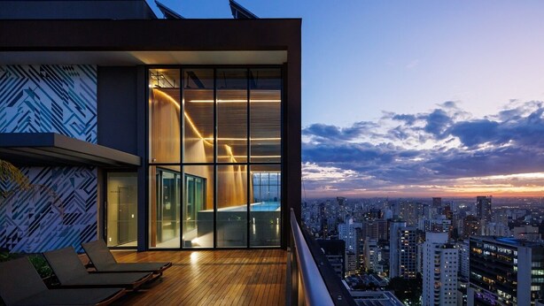 A modern building with large windows, a wooden deck, and a cityscape view at dusk. - Apto Próximo Oscar Freire e Rebouças (Pinheiros São Paulo)