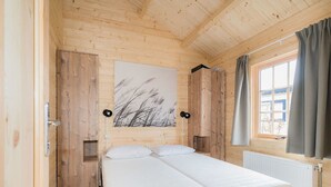 Et værelse i en træhytte med en seng, et vindue med gardiner og en lampe på væggen.