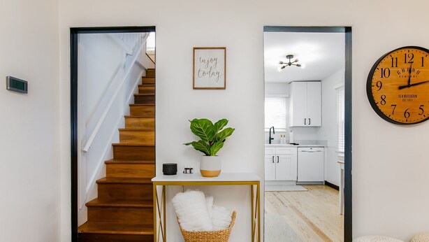 A staircase leading to a kitchen with white cabinets, a clock, and a framed sign on the wall.