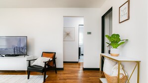 A modern living room with a television, a comfortable chair, a white console table, a potted plant, and a framed inspirational quote on the wall.