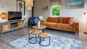 A modern living room with a sofa, TV, wooden coffee table, and a fireplace. - Holiday Home Near Dunes With Wellness Garden (Den Burg)