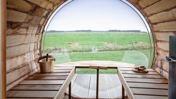 A circular wooden structure with a bench and a table, a bucket, and a plate with food items. - Holiday Home Near Dunes With Wellness Garden (Den Burg)