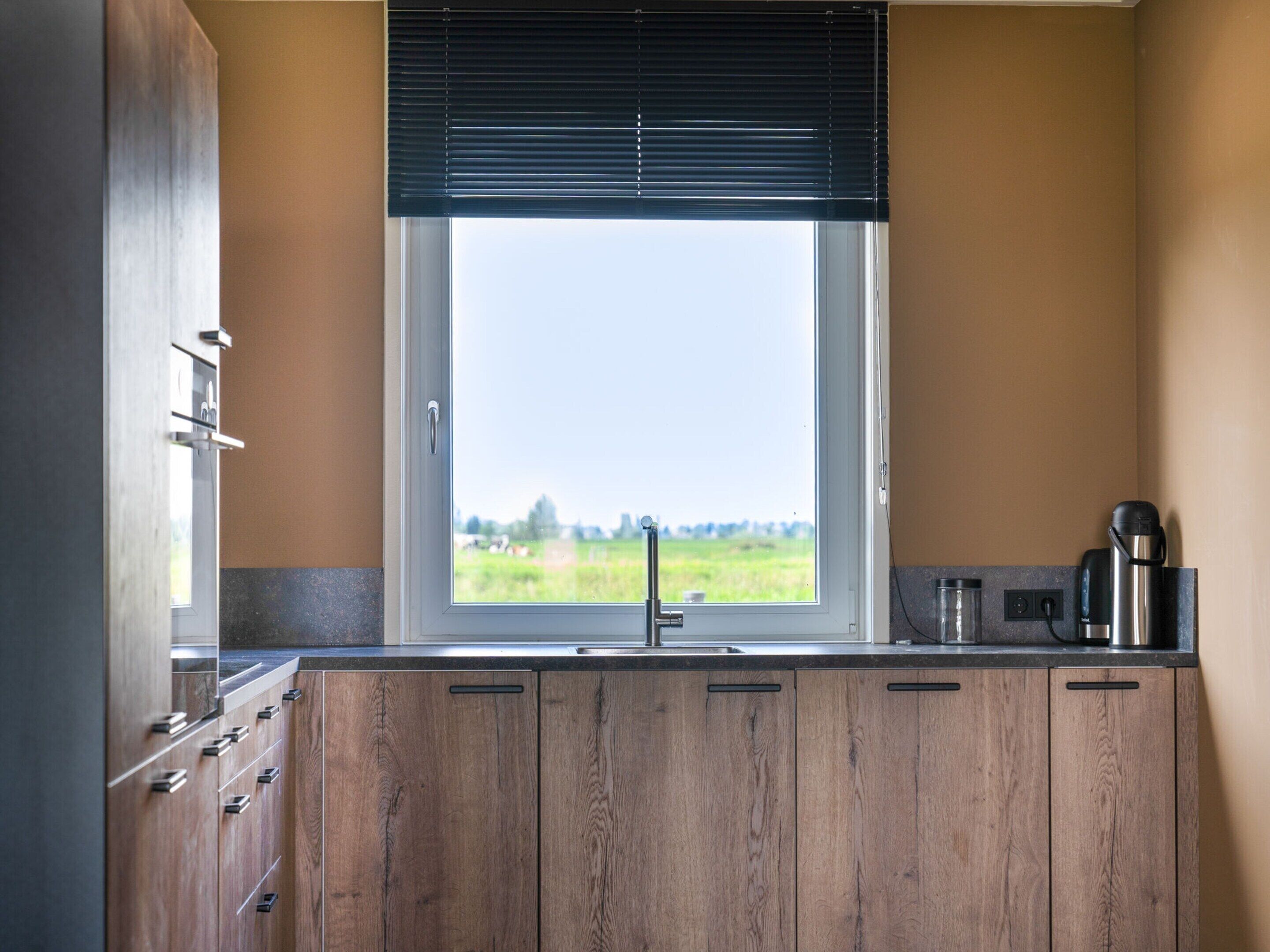 A kitchen with wooden cabinets, a window with a view of greenery, and a coffee maker on the counter.
