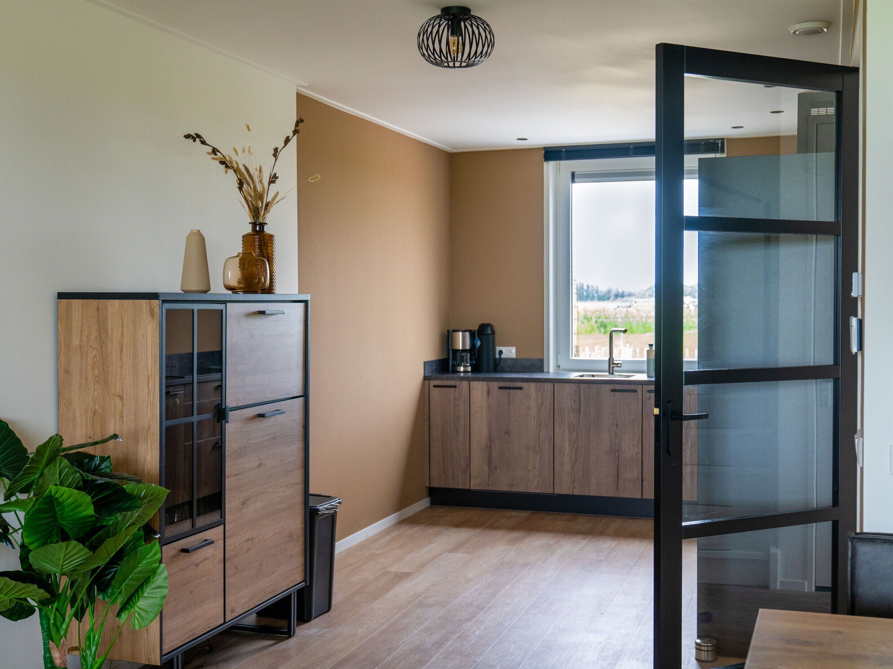 A modern kitchen with wooden cabinets, a coffee machine, and a view through a glass door.