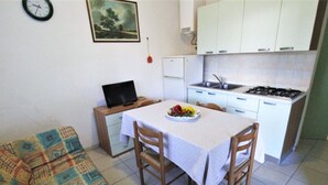 Ett litet, kompakt bostadsutrymme med ett minikök, ett matbord med stolar, en soffa och en tv som står på ett sidobord.