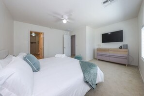 Een slaapkamer met een groot bed, een plafondventilator, een televisie aan de muur en een dressoir.