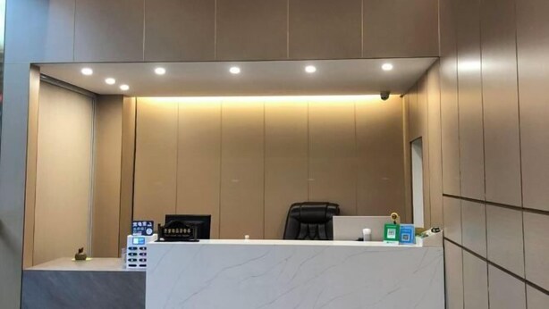 A reception area with a marble counter, a black office chair, a desk with a computer and a phone, and a wall-mounted clock. - Cangnan Water View Hotel (Cangnan)