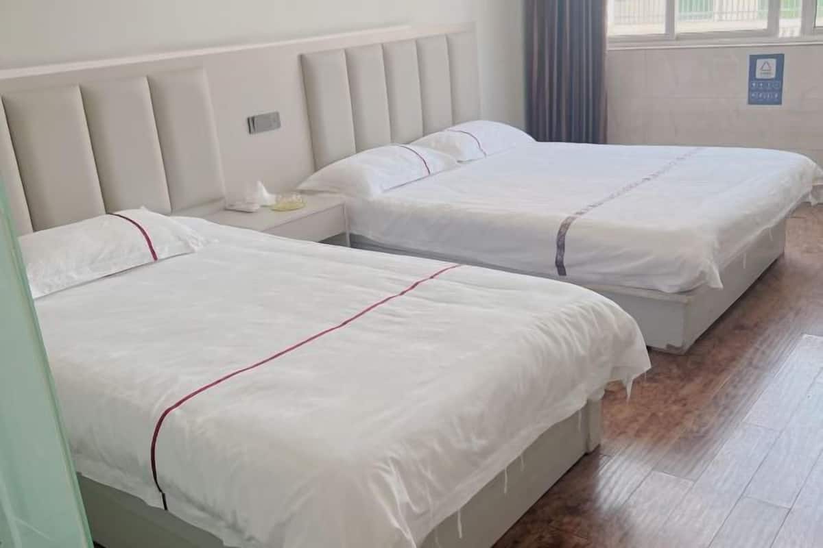 Ein Hotelzimmer mit zwei Betten, einem Nachttisch und einem Fenster mit Vorhängen.
