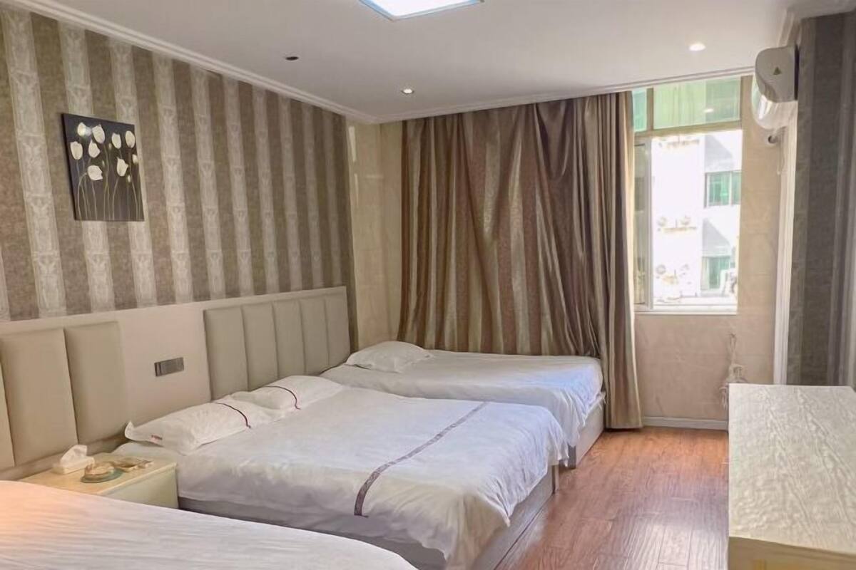 Ein Hotelzimmer mit zwei Betten, einem Nachttisch, einem Fenster mit Vorhängen und einer Wand-Klimaanlage.