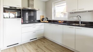 A modern kitchen with white cabinets, a black countertop, and a window providing natural light. - Holiday Home in Scherpenisse Near Oosterschelde (Scherpenisse)