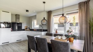 A modern kitchen with white cabinets, a black countertop, and a dining area with a wooden table and grey chairs. - Holiday Home in Scherpenisse Near Oosterschelde (Scherpenisse)