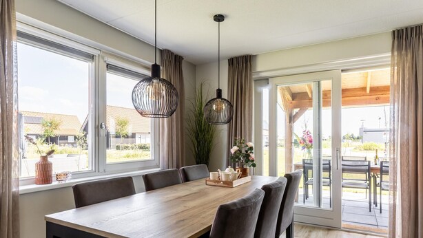A dining area with a wooden table, six chairs, hanging pendant lights, and a view of the outdoors through large windows. - Holiday Home in Scherpenisse Near Oosterschelde (Scherpenisse)