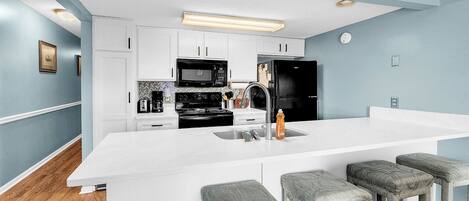 A modern kitchen with white cabinetry, a black refrigerator, a microwave, and a large island with bar stools.