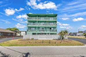 A multi-story building with balconies, a parking area, and a clear sky.