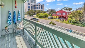 Un balcon donnant sur une rue, une maison rouge et un immeuble en arrière-plan.