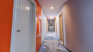 A hotel hallway with a carpeted floor, white doors, and orange walls. - Shankee Chain Hotel (Guangzhou North Station Huacheng Road Subway Station) (Guangzhou)