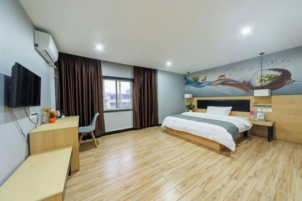 A hotel room with a bed, desk, chair, and a mural on the wall.