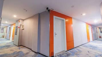 A hotel corridor with a patterned carpet, a white door, and a security camera.