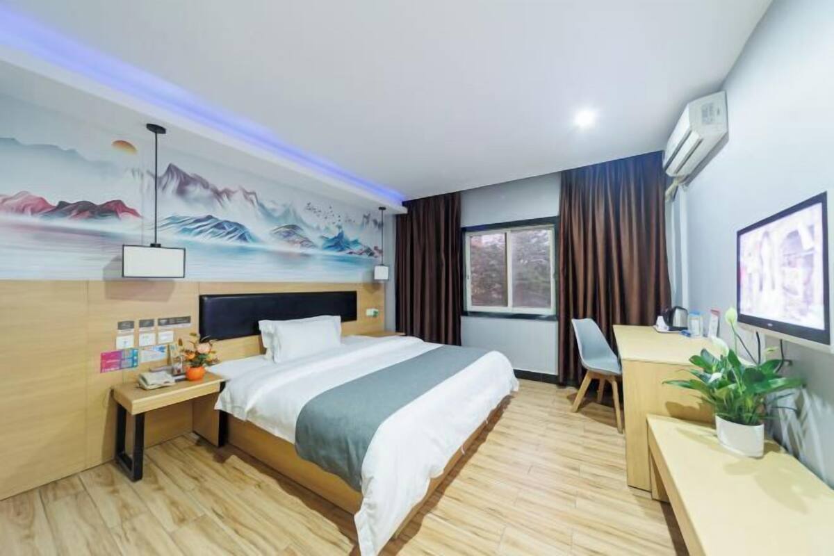 A hotel room with a bed, desk, chair, and a painting on the wall.