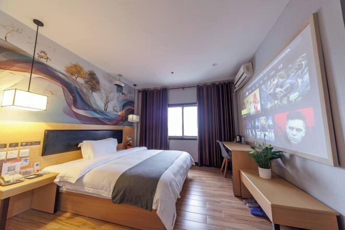 A hotel room with a bed, desk, and a large screen displaying a movie.