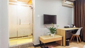 A hotel room with a glass shower enclosure, a TV mounted on the wall, a desk with a chair, and a small potted plant. - Shankee Chain Hotel (Guangzhou North Station Huacheng Road Subway Station) (Guangzhou)