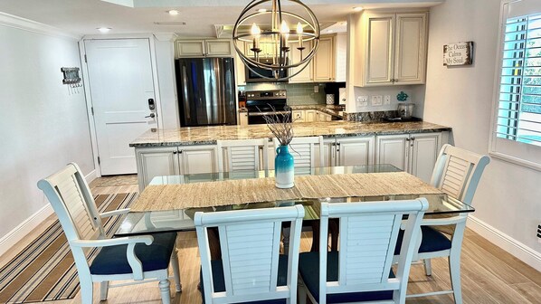 A modern kitchen with white cabinetry, a stainless steel refrigerator, and a glass dining table with chairs.