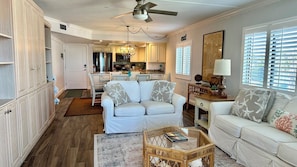 A spacious living room with a white sofa, a coffee table, and a dining area with a kitchen in the background. - Gulf View! Peace & Serenity @ Sandpiper Beach 501. (Sanibel)