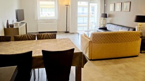 A modern living room with a dining table, sofa, and a TV on a stand. - Apartment in Nieuwpoort Near the Beach (Nieuwpoort)