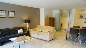 A living room with a sofa, a coffee table, and a dining area with chairs. - Apartment in Nieuwpoort Near the Beach (Nieuwpoort)