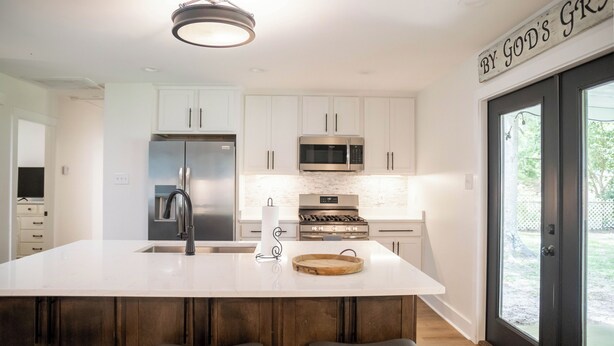 A modern kitchen with white cabinets, stainless steel appliances, and a large island with stools. - With GOLF CART! 1 mile ride to the beach & Downtown Ocean Springs! Clark Cottage (Ocean Springs)