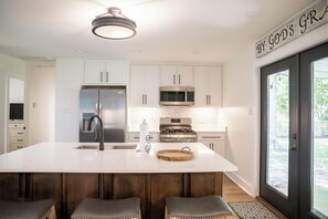 Una cocina moderna con gabinetes blancos, electrodomésticos de acero inoxidable y una isla grande con taburetes.