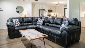 A modern living room with a black leather sectional sofa, a wooden coffee table, and a ceiling fan. - With GOLF CART! 1 mile ride to the beach & Downtown Ocean Springs! Clark Cottage (Ocean Springs)