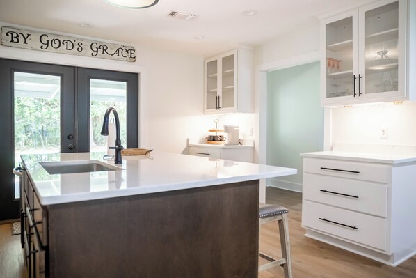 Cocina moderna con una isla central, armarios blancos y un cartel sobre la puerta.