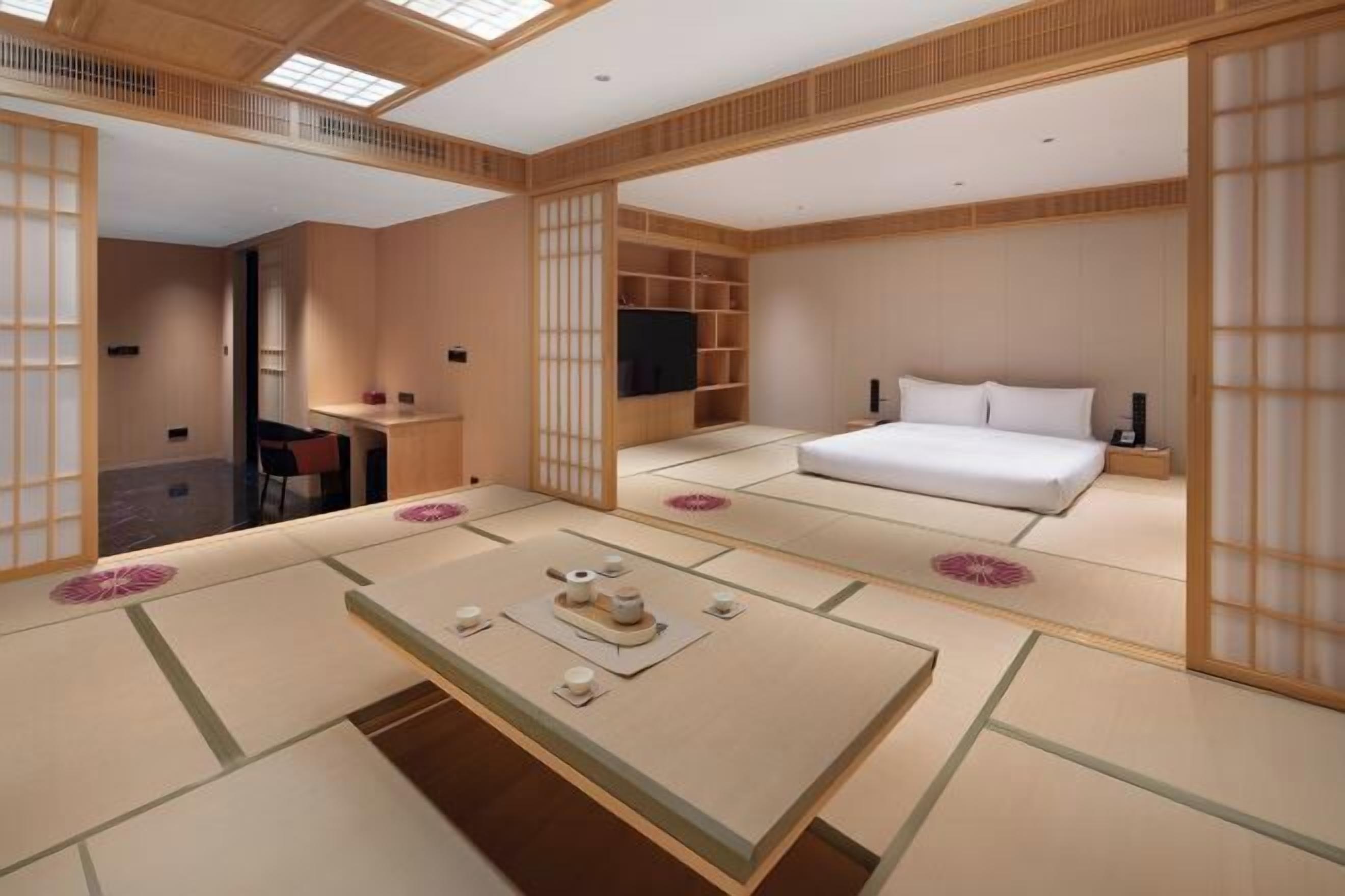 A traditional Japanese-style room with tatami flooring, a bed, a TV, and a sliding door.