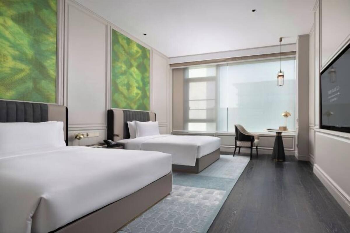 A hotel room with two beds, a desk, a chair, and a large window.