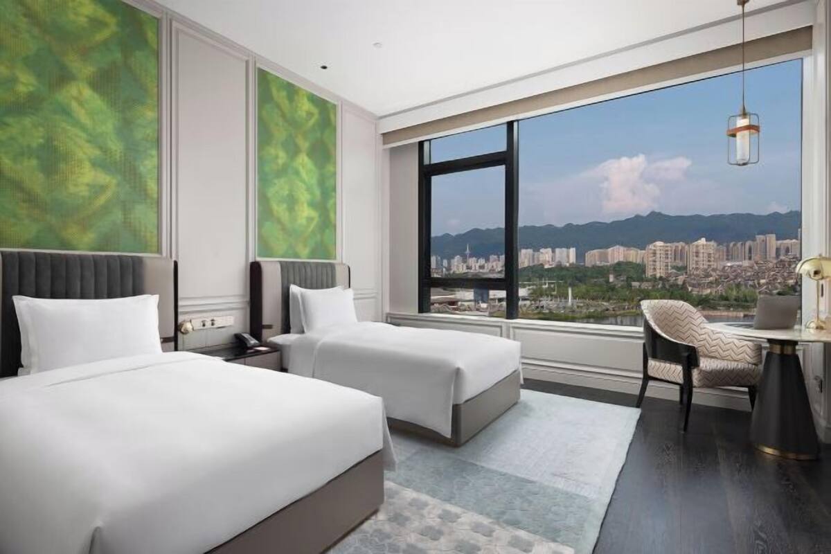A hotel room with two beds, a city view, and a large window.
