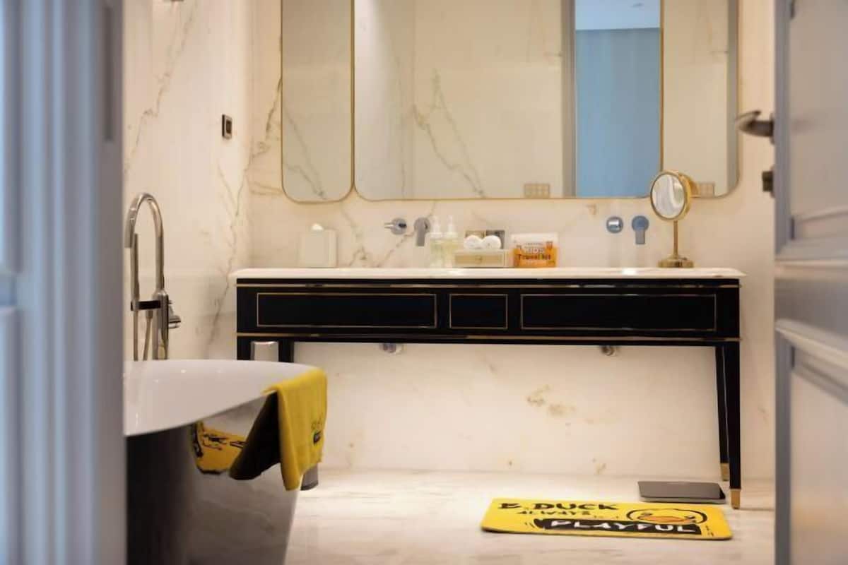 A bathroom with a marble wall, a sink with a mirror, and a yellow caution sign on the floor.