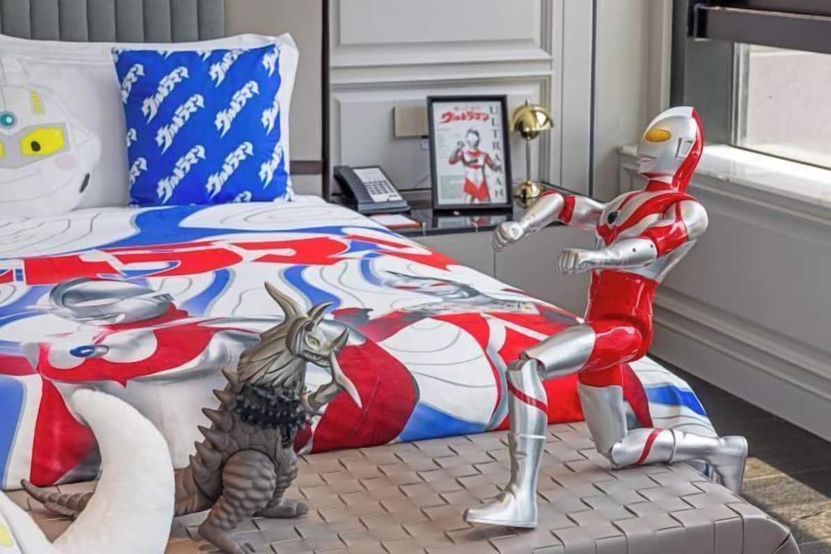 A bedroom with a bed featuring a superhero-themed bedspread, a small statue of a robot, and a framed picture on the nightstand.
