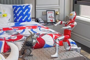 A bedroom with a bed featuring a superhero-themed bedspread, a small statue of a robot, and a framed picture on the nightstand.
