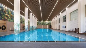 En indendørs swimmingpool med træloft, søjler og et muralmaleri på væggen.