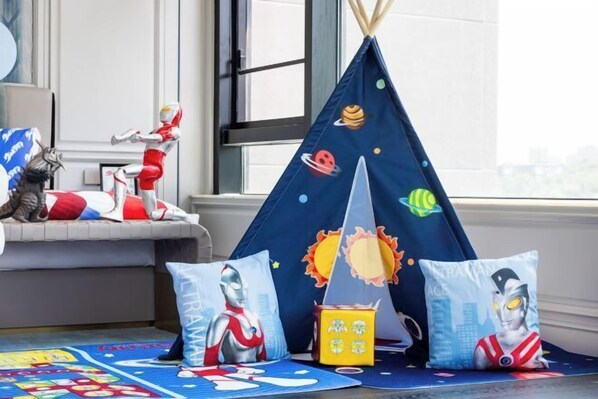 A room with a space-themed tent, pillows with space and robot designs, and a play mat with cartoon characters.