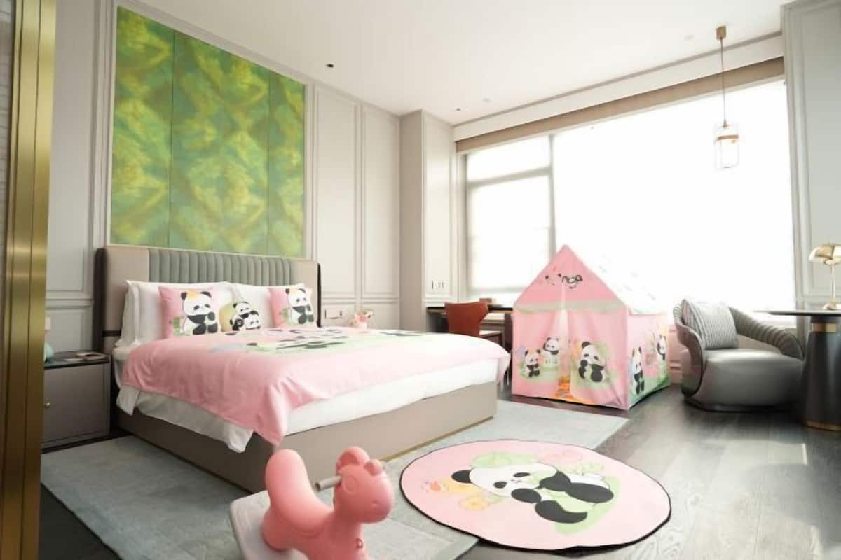 A bedroom with a bed, a pink play tent, a panda-themed rug, and a window with natural light.